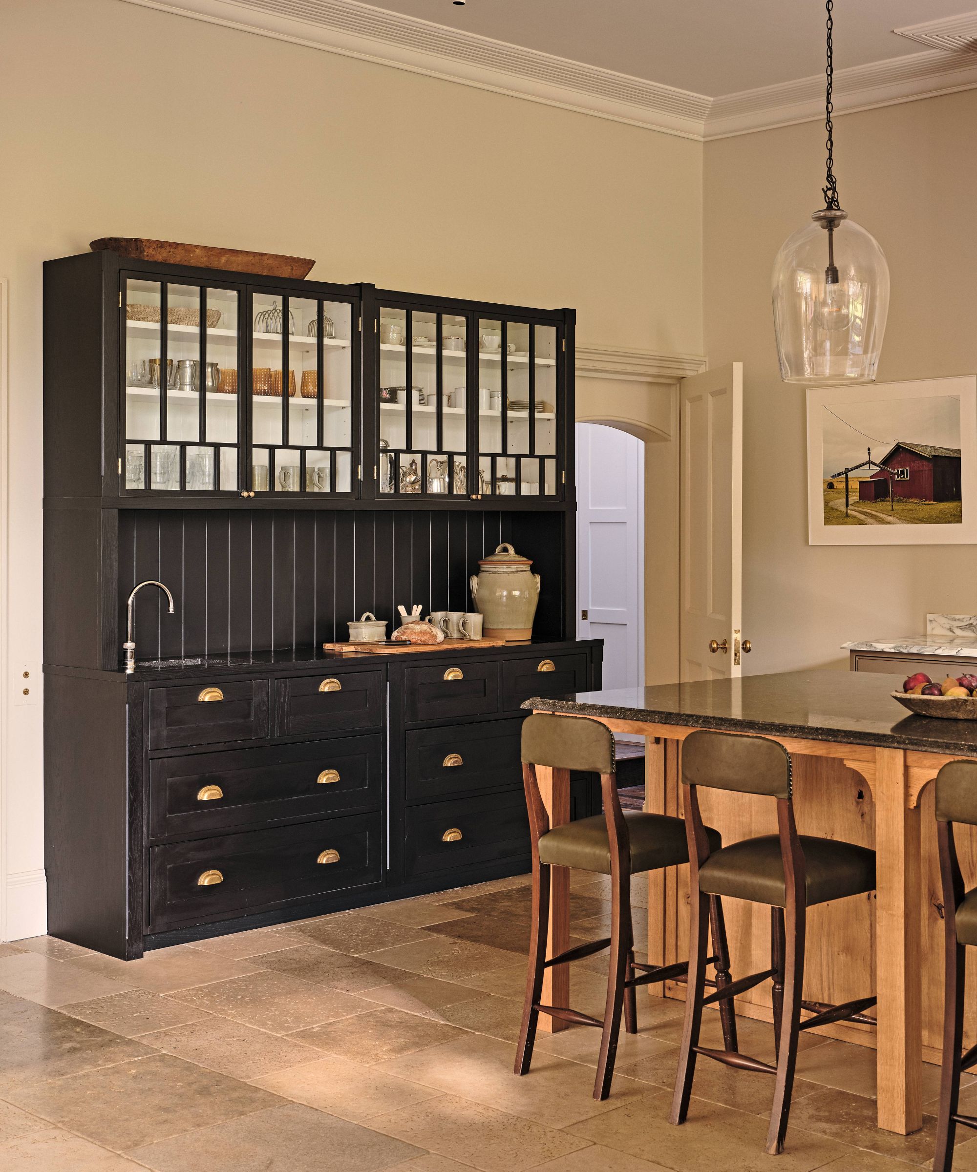 a warm beige painted kitchen with an oak wooden island, a black vintage credenza style unit with mini sink and crockery storage