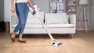 A cordless vacuum cleaner being pushed through the living room with a sofa behind