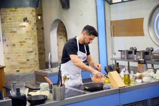 Craig Doyle at his workstation in the Celebrity MasterChef kitchen, making a slaw, with his hand in a bowl of grated root vegetables