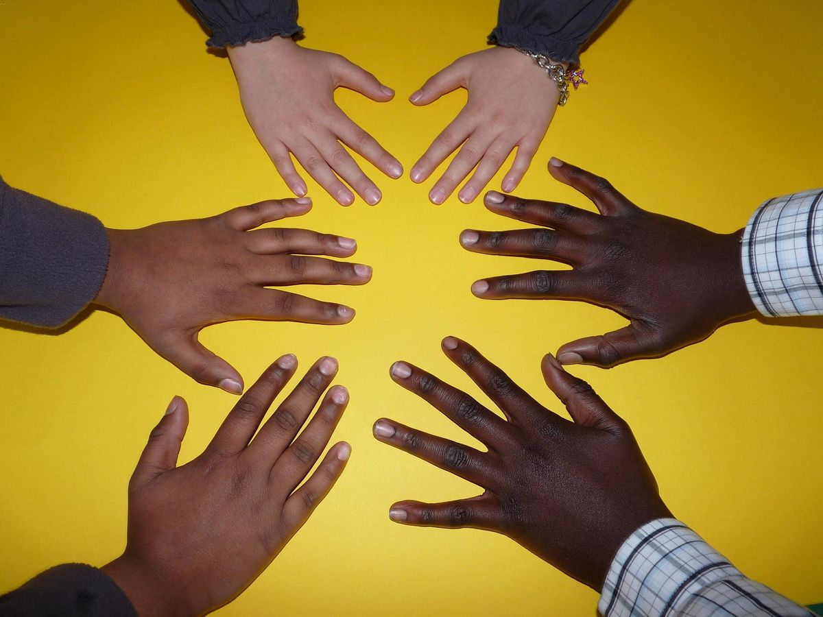 Three hands palm down in a circle against a yellow background