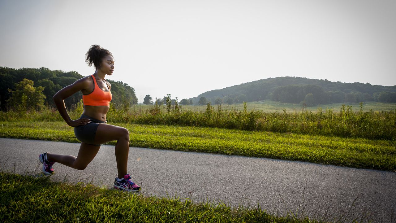 Young female runner stretching on rural park path