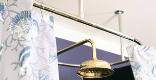 Blue bathroom with blue patterned shower curtain surrounding a gold shower head