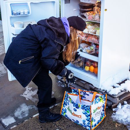 woman in snow in front of community fridge