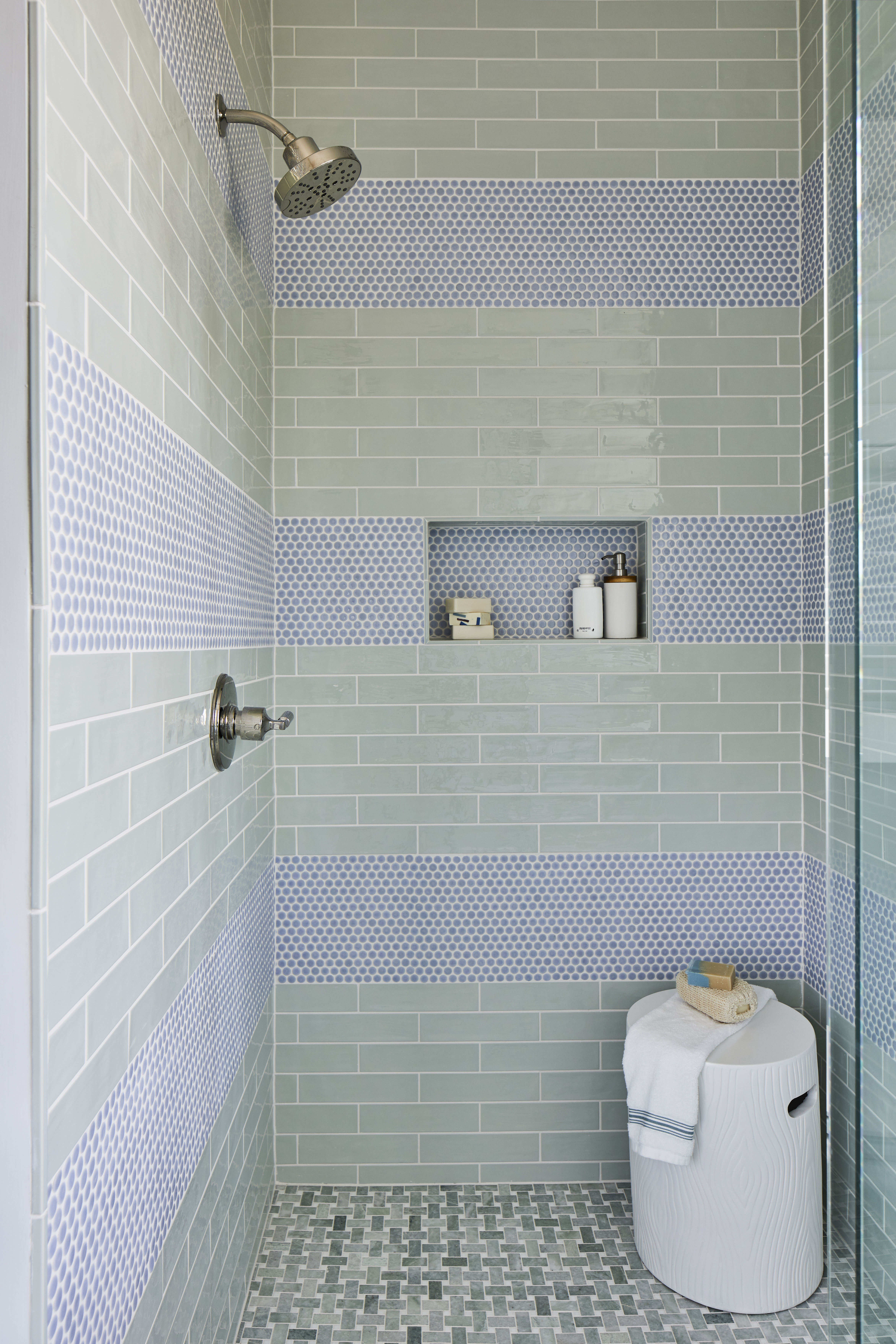 A blue and green-tiled shower with a small white table and a recessed shelf.