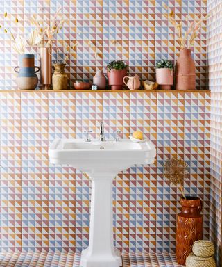 Heavily patterned tile on both floor and wall to frame white basin and wall shelf with ceramics and greenery