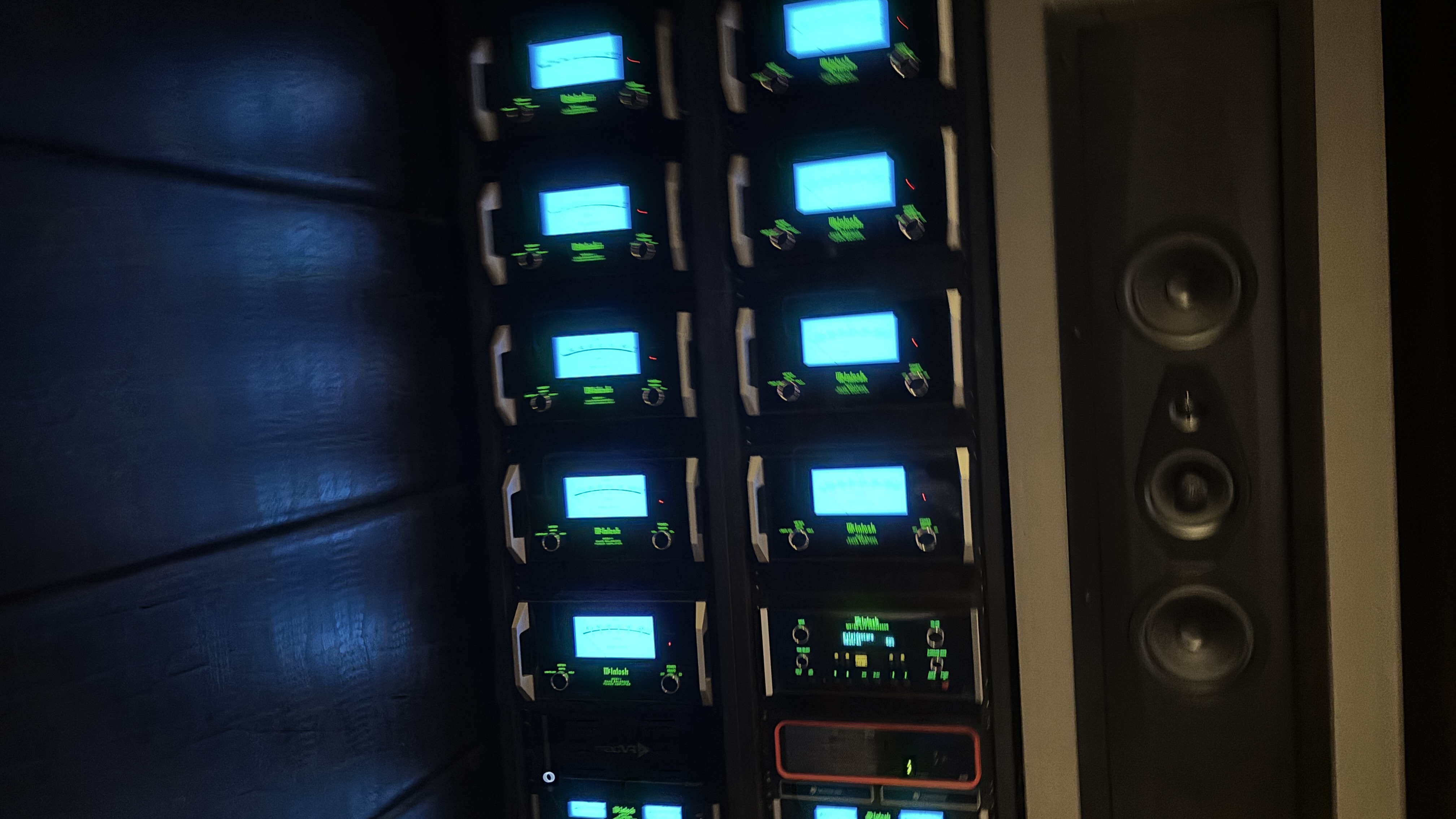 A stack of McIntosh amplifiers in a rack next to a Sonus Faber surround speaker