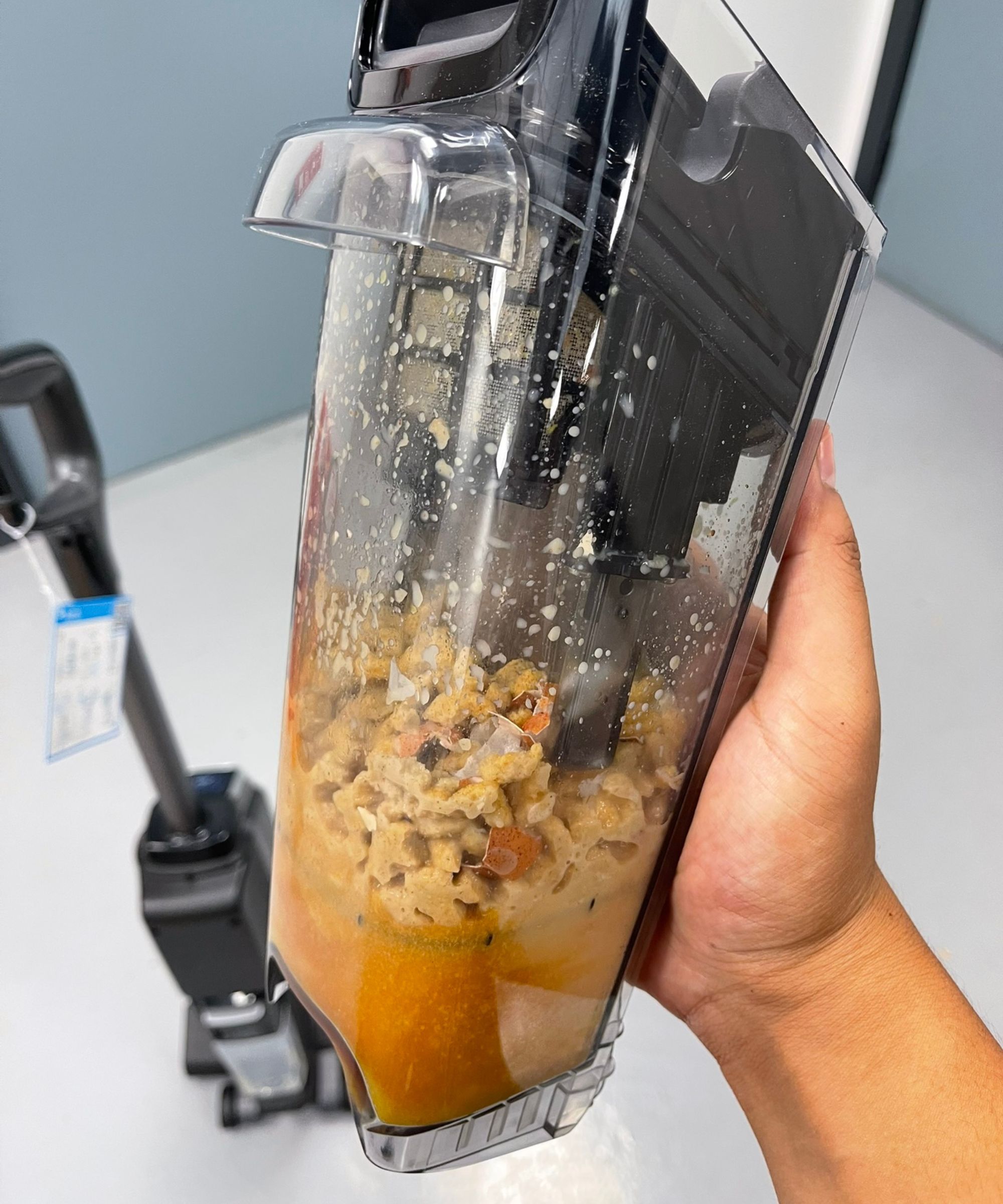 Hand holding the Bissell CrossWave OmniForce Edge dirty tank showing food and dirty liquid.