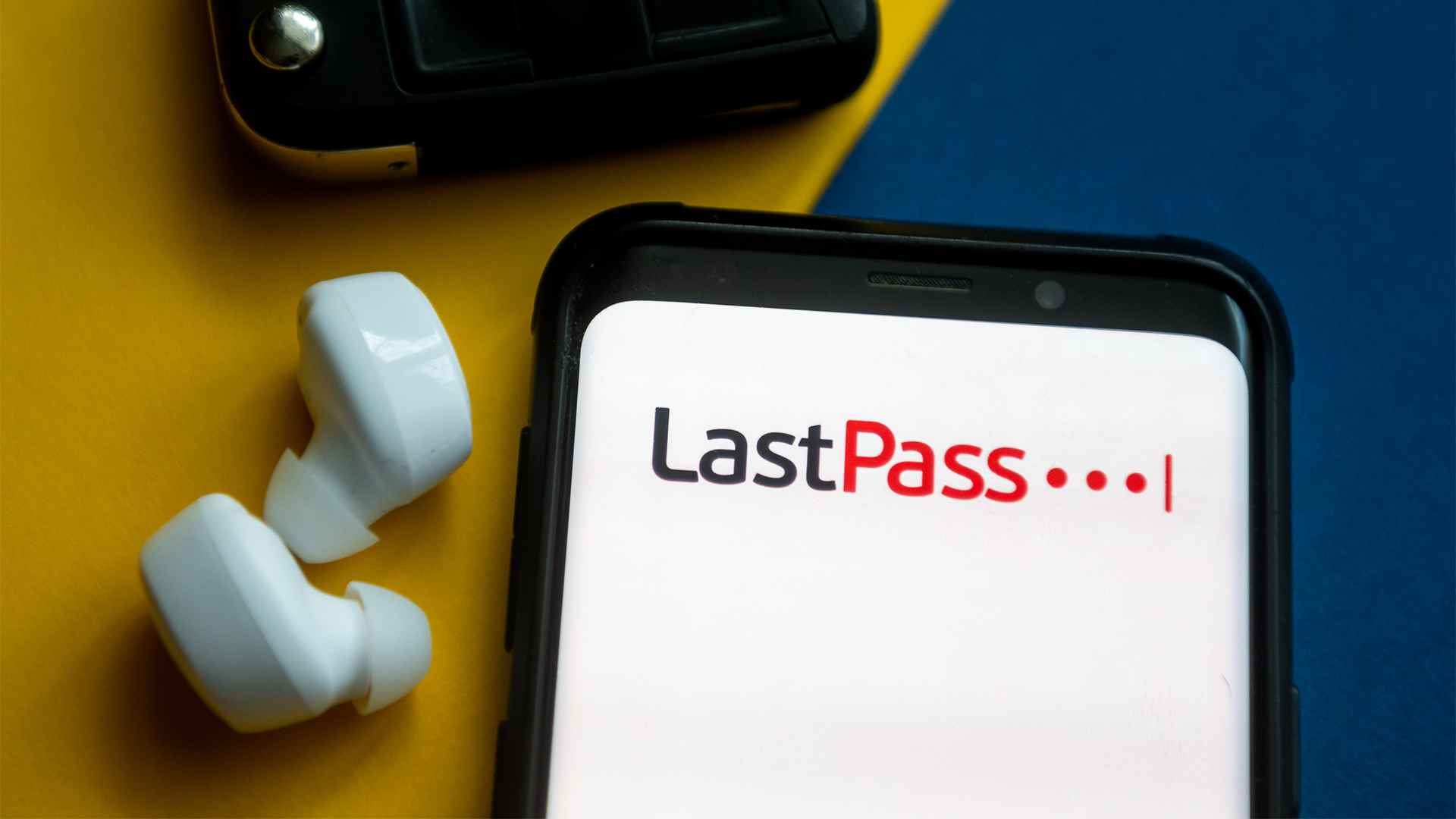 LastPass logo and branding pictured on a smartphone screen with car key and earbuds sat next to smartphone.
