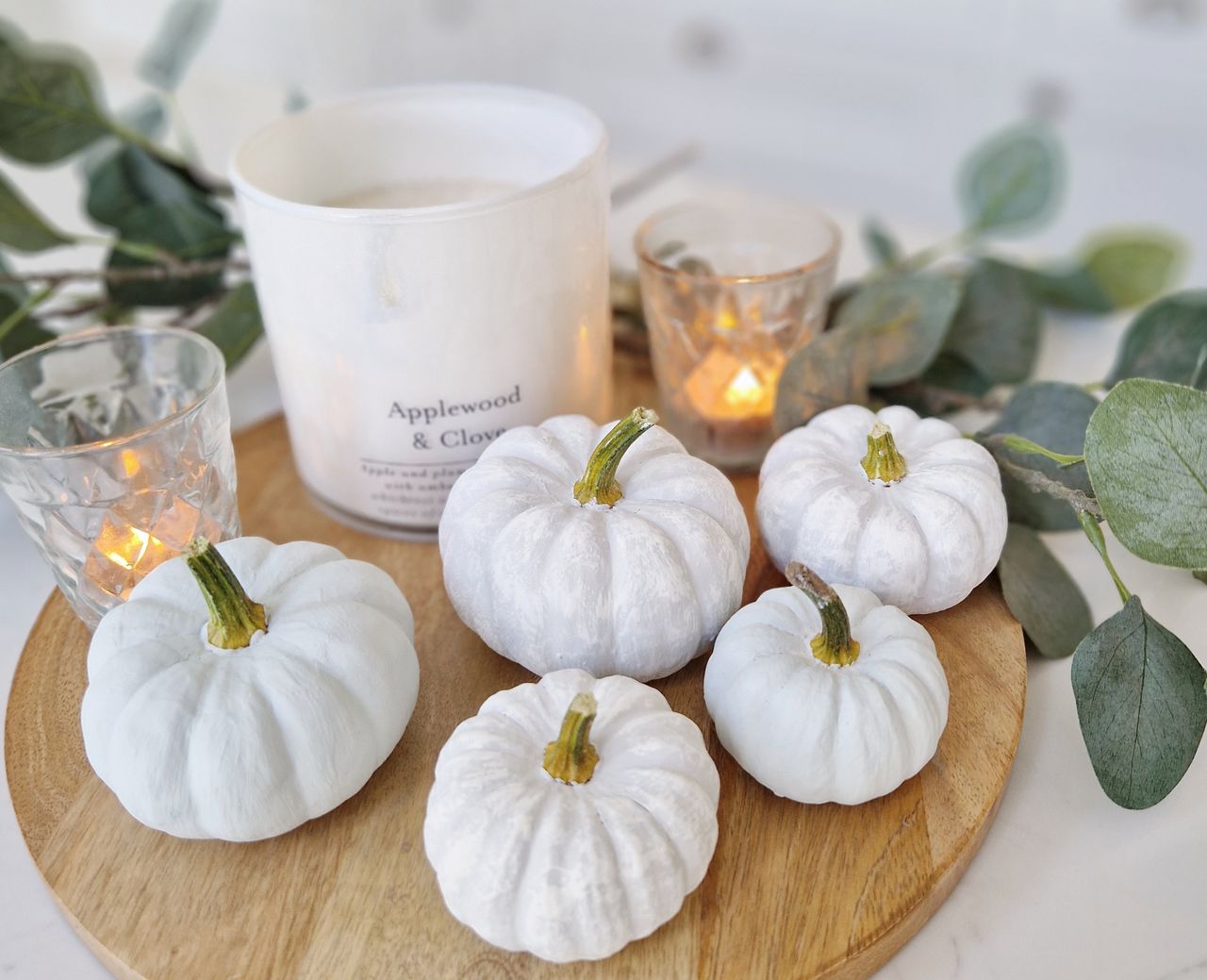 A selection of mini pumpkins painted white arranged next to a cande