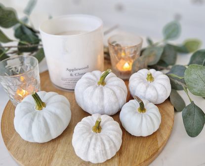 A selection of mini pumpkins painted white arranged next to a cande