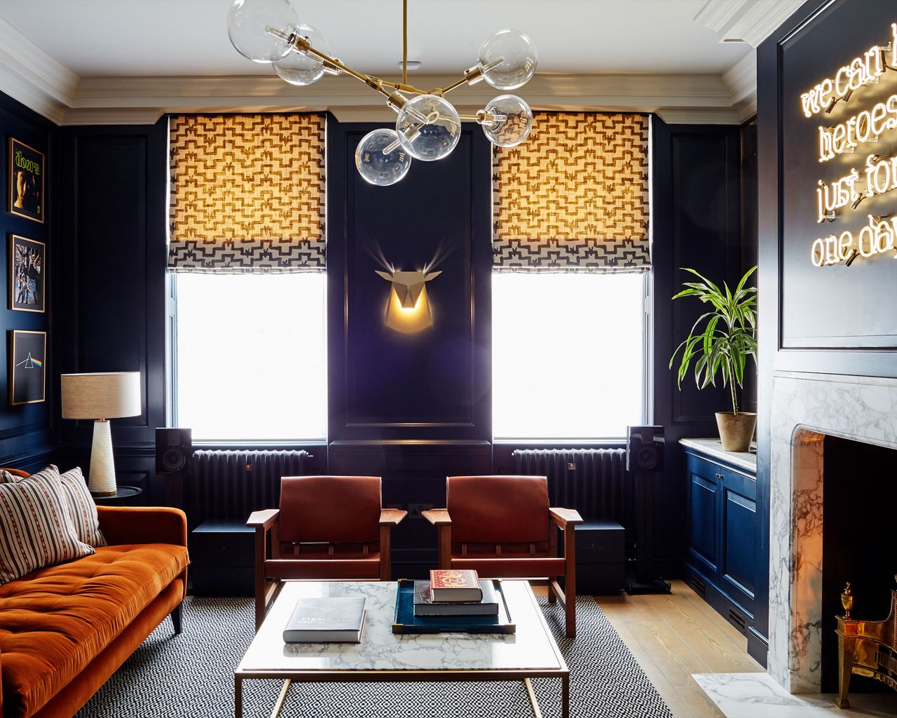 Living room with dark blue wood panelled walls, fireplace with marble surround and neon light on the chimney breast, a David Bowie lyric We can be Heroes Just For One Day.