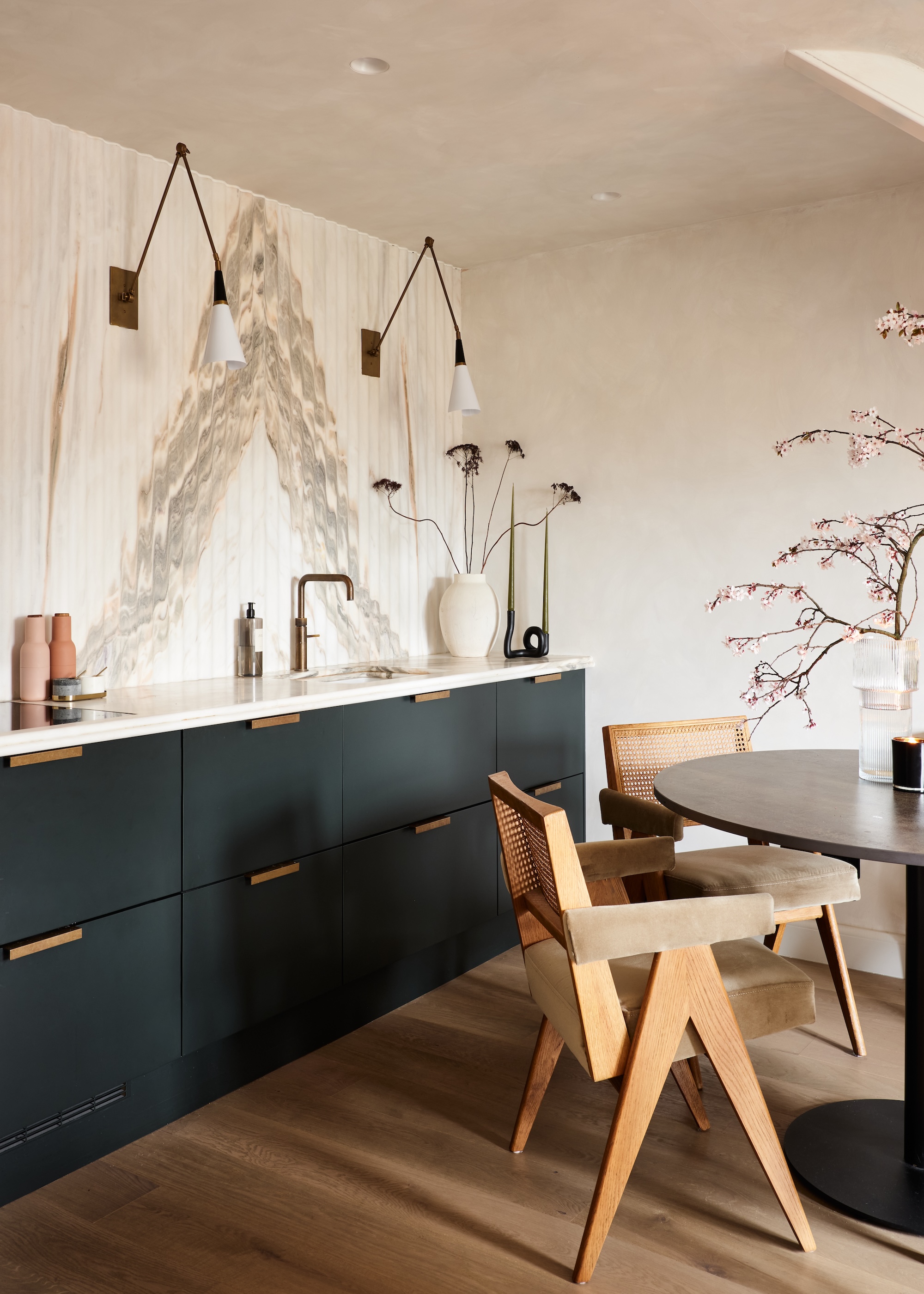 A small kitchen with deep green cabinets and a glass dining table in the middle with chairs beside the dining table