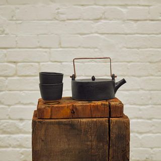 Kettle and cups on a stand with a white brick wall behind