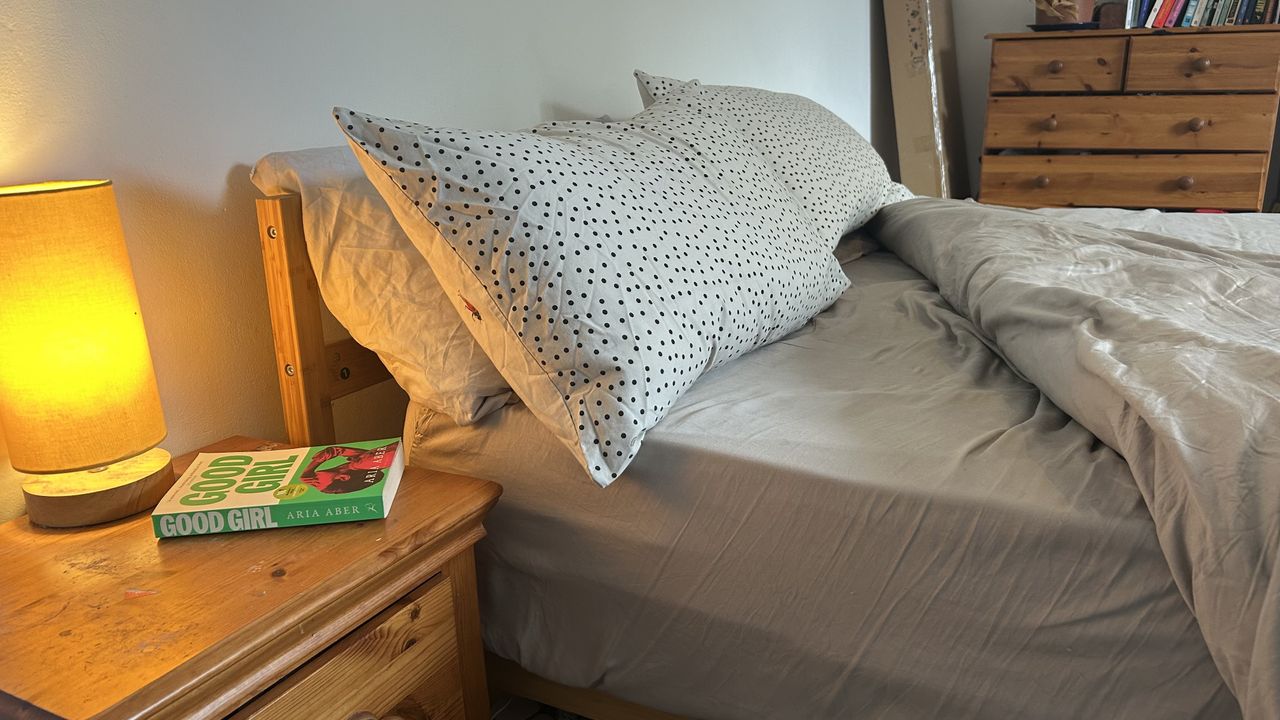 The Awara Classic mattress dressed in grey bedding with a lamp on a bedside table next to it
