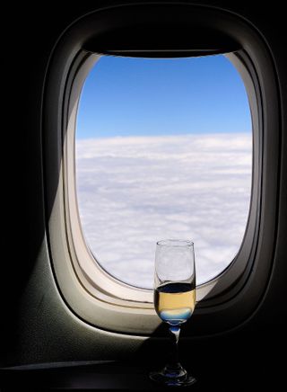A glass of champagne set against an airplane window showing the clouds and sky.