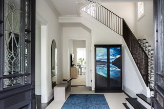 A mostly monochrome modern entryway with blue accents in the rug and a mural on the cupboard doors