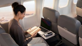 Anker power bank on aeroplane tray table with laptop and person reading a book