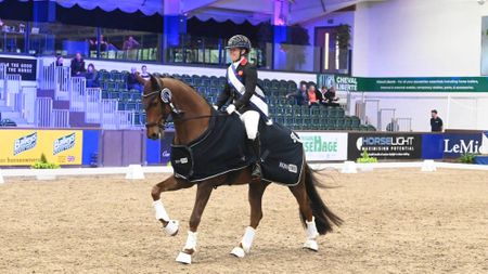 woman riding a horse at a canter. She wears a winners sash and the horse wears a winners rug