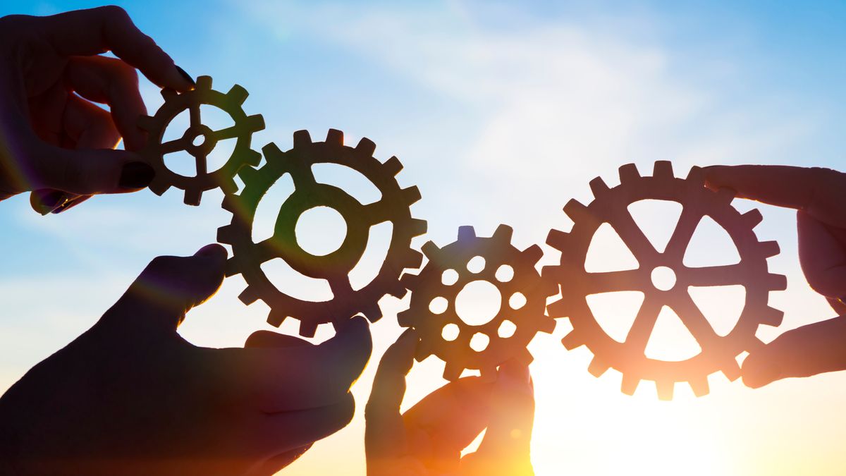 Four people holding up gears to show collaboration, against a blue sky 