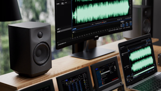 Lifestyle image of the FiiO SP5 active speakers. The speaker is atop a music studio desk with a monitor to its right and a laptop on the lower level just below and in front of the monitor