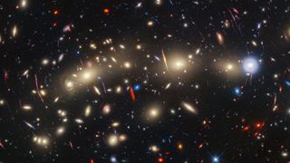 We see an array of twinkling yellow, red, and blue galaxies stretched across space in a way that is reminiscent of Christmas lights