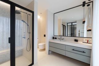 neutral modern bathroom with black fixtures and fittings, cream stone floor, shower with mosaic wall and shower bench, black shower doors