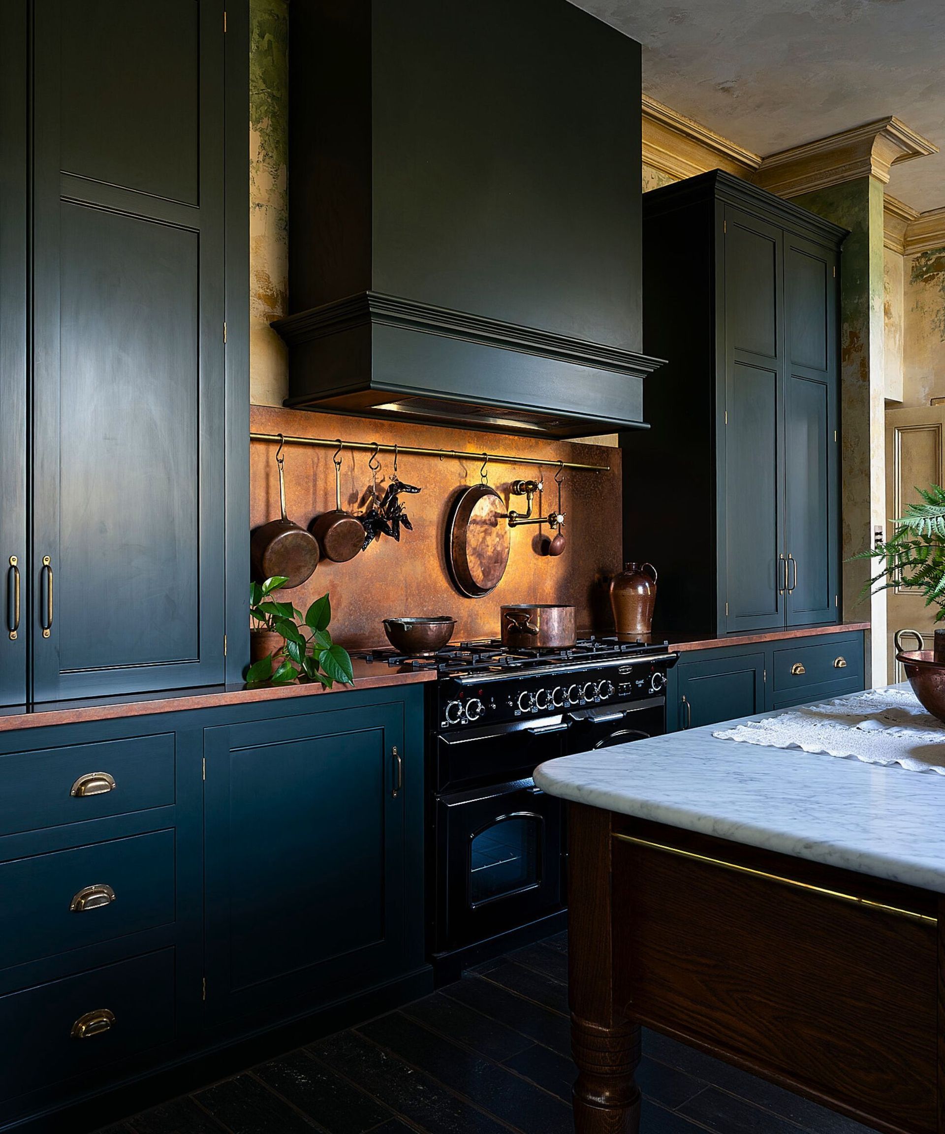 A dark green kitchen with copper splashback and worktop