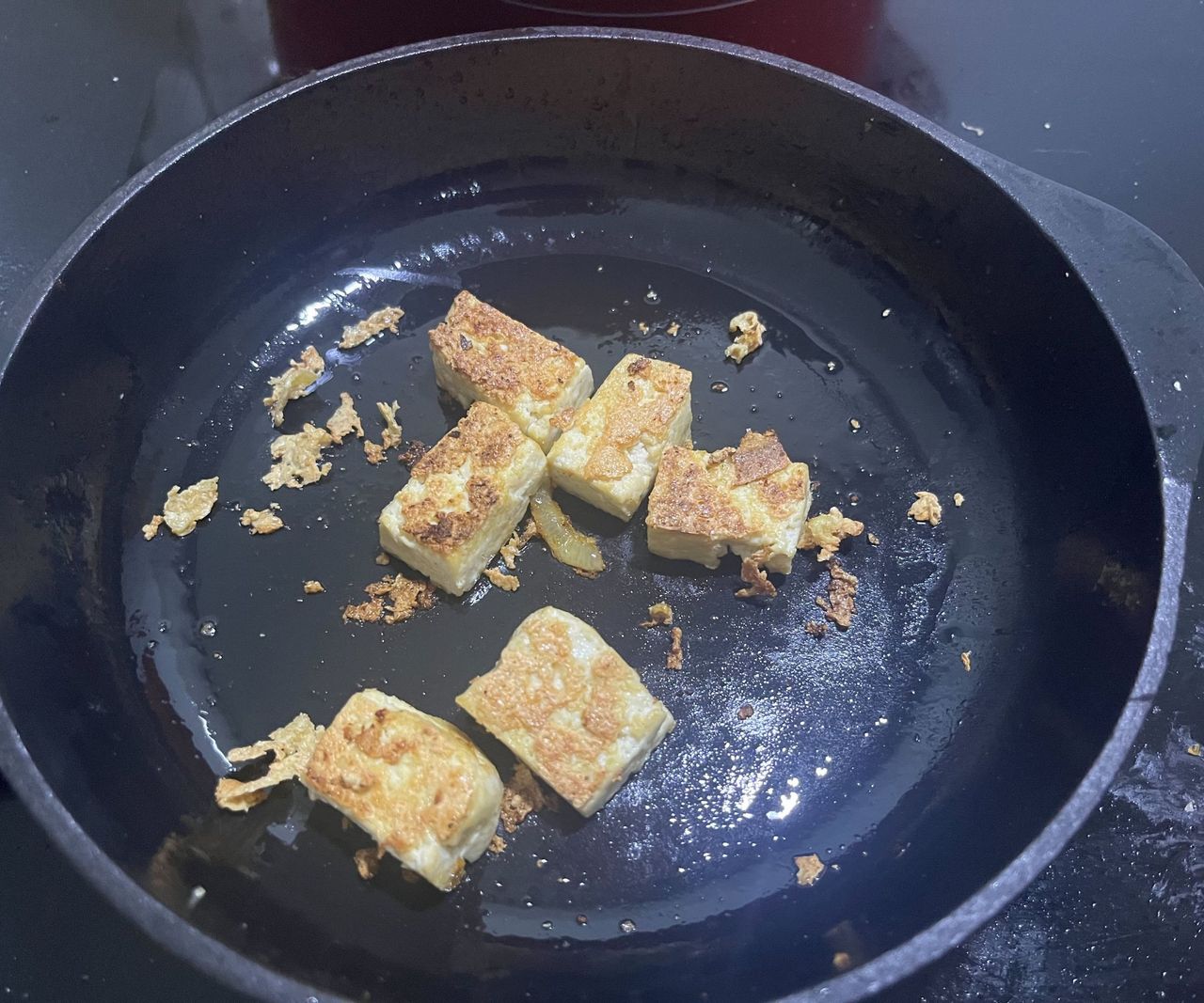 Tofu frying in a a small black cast iron skillet.