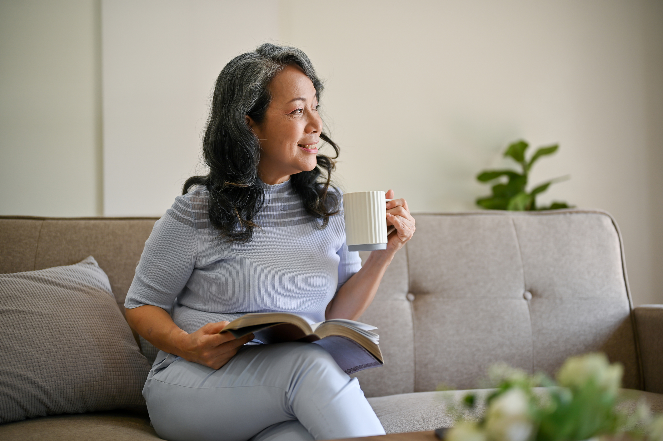 Philippine woman sitting on a couch, drinking coffee with a book