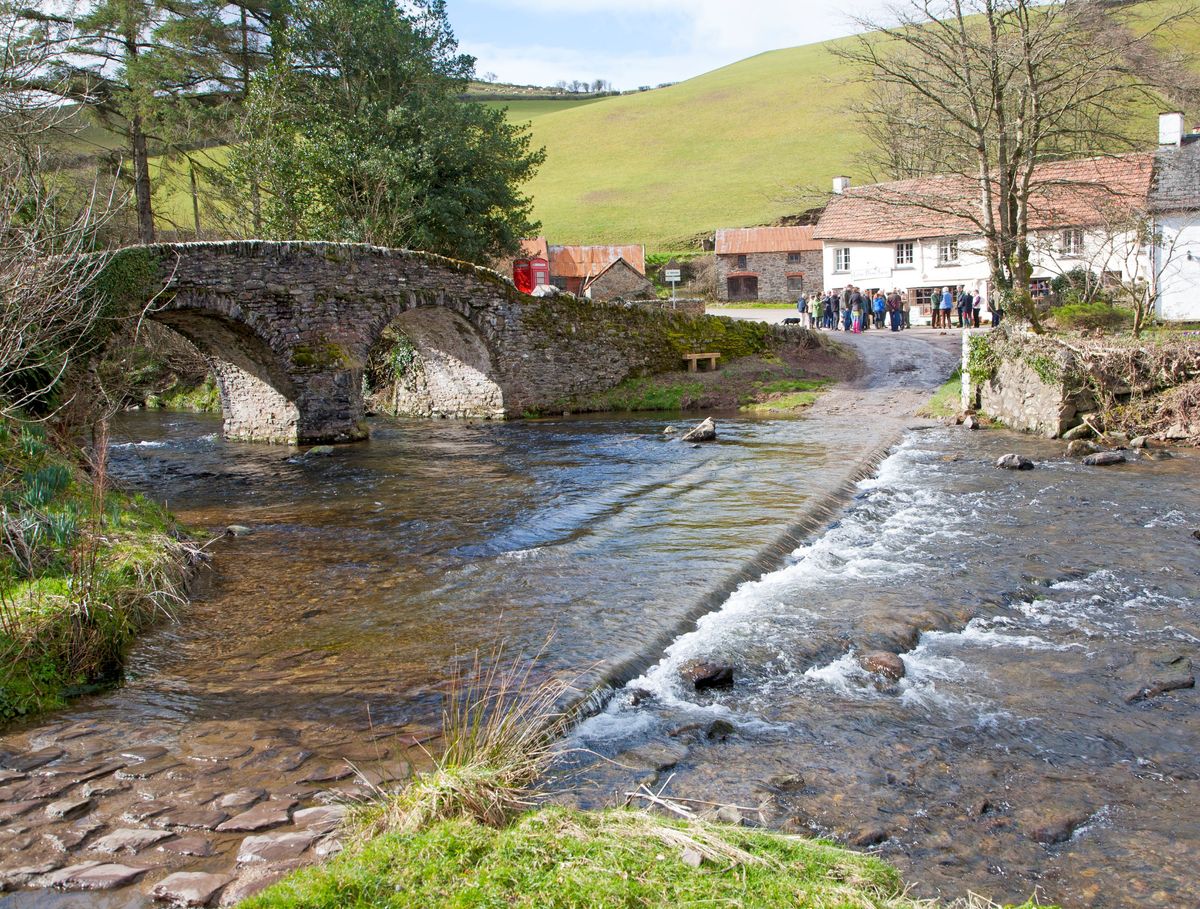 A river in front of a countryside cottage with a bridge in the foreground