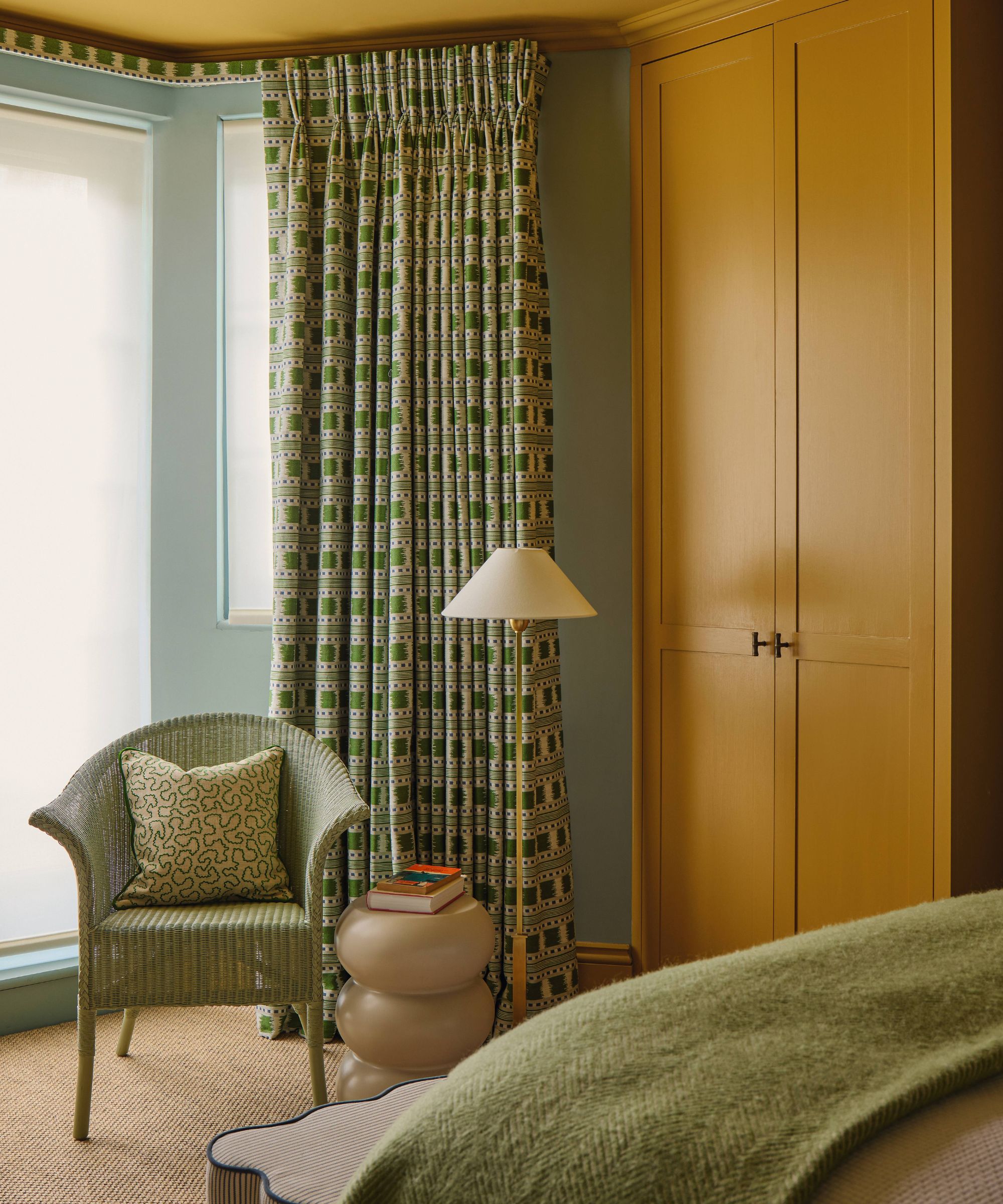 a bright yellow and green bedroom with bay window styled with green checkered drapes, a small wicker chair with side table and floor lamp