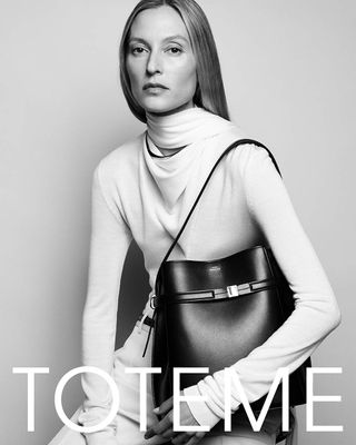 A model wearing a contemporary white dress and carrying a black bag from Toteme