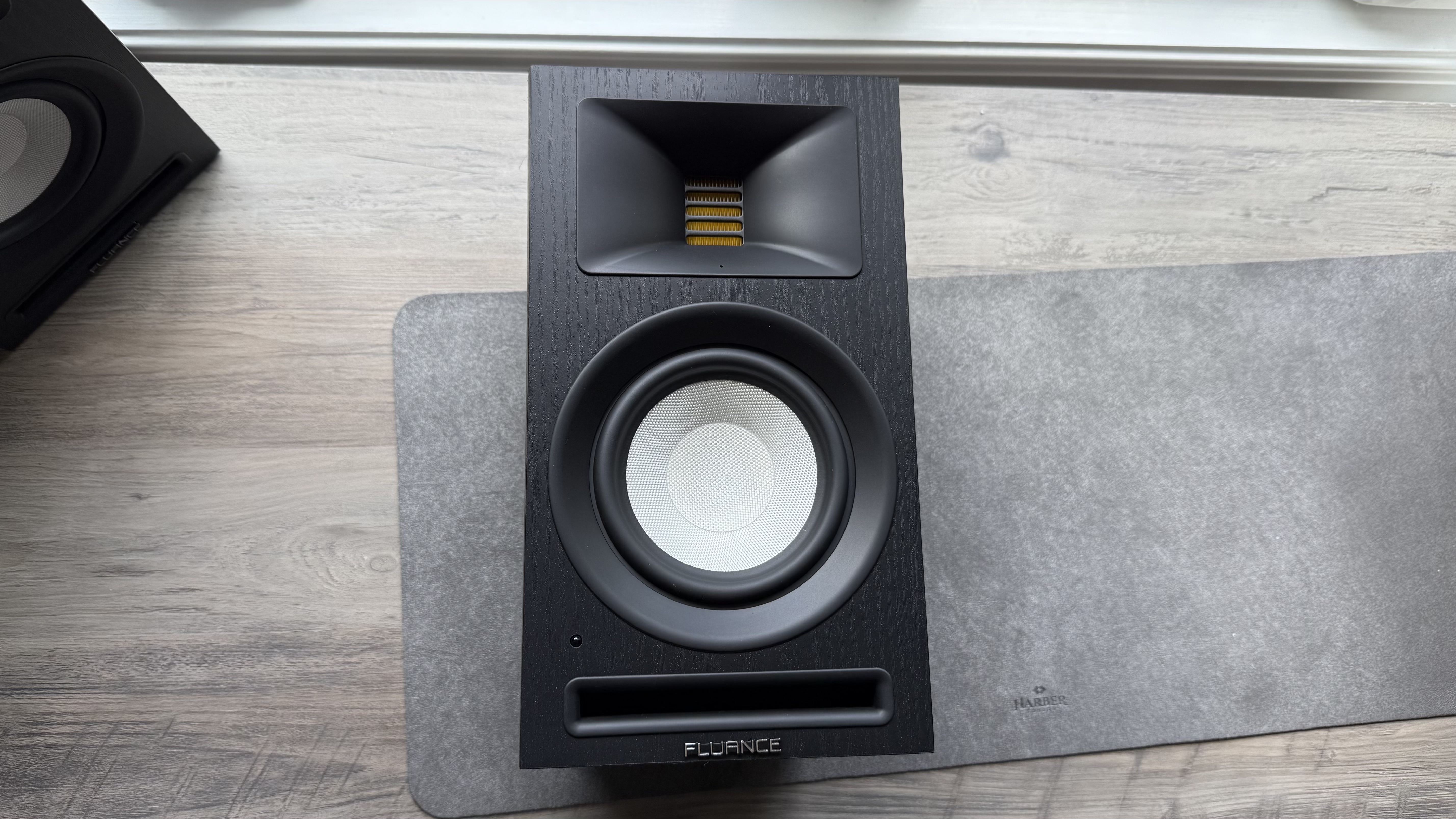 Front panel of the Fluance Ri71 powered bookshelf speaker, placed on its back on a matt, on a wooden surface.