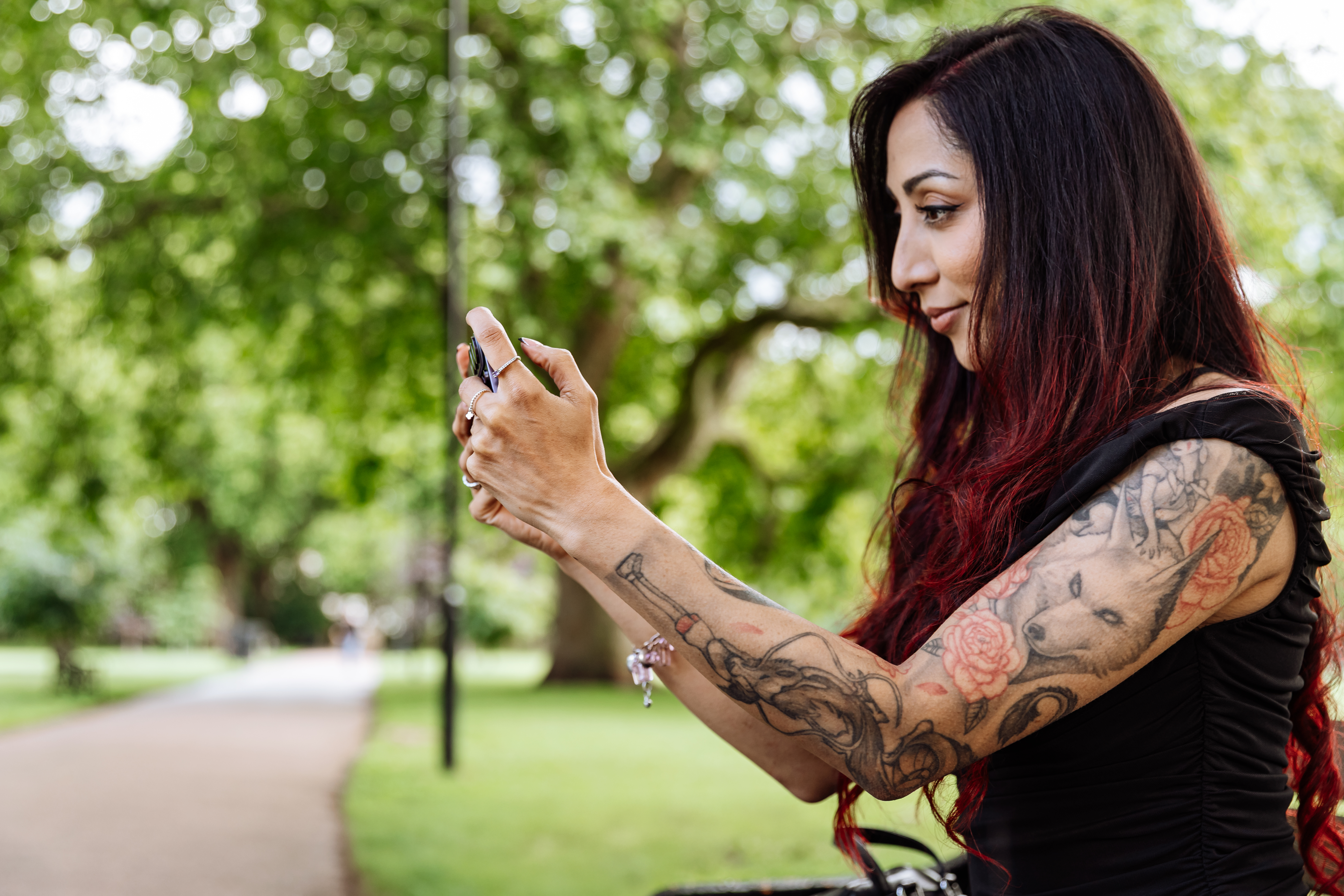 A lady holds a Samsung Galaxy S26 Ultra phone while sitting on a bench in a park