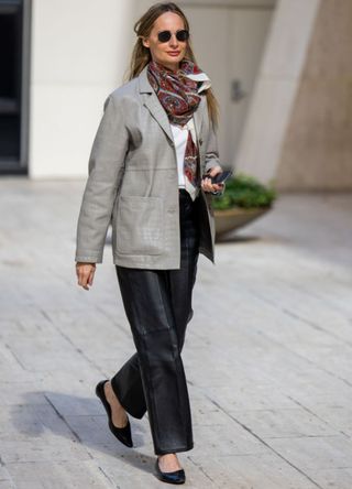 A woman in New York wearing an oversized grey jacket, leather trousers and a paisley pattern scarf.