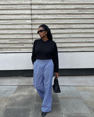 London woman wears blue striped pajama style pants, black v-neck sweater, sunglasses and Chanel flats.