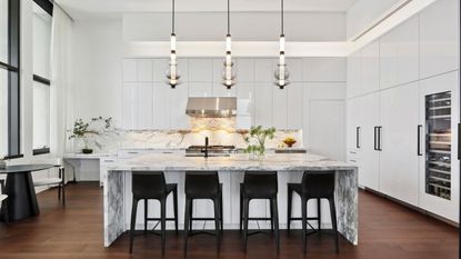 Modern white kitchen with large marble island and black high chairs