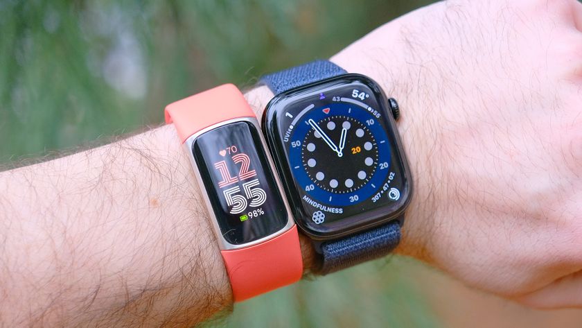 Close up of a Fitbit Charge 6 with an orange band on a user&#039;s wrist next to an Apple Watch 10 with an out-of-focus green background