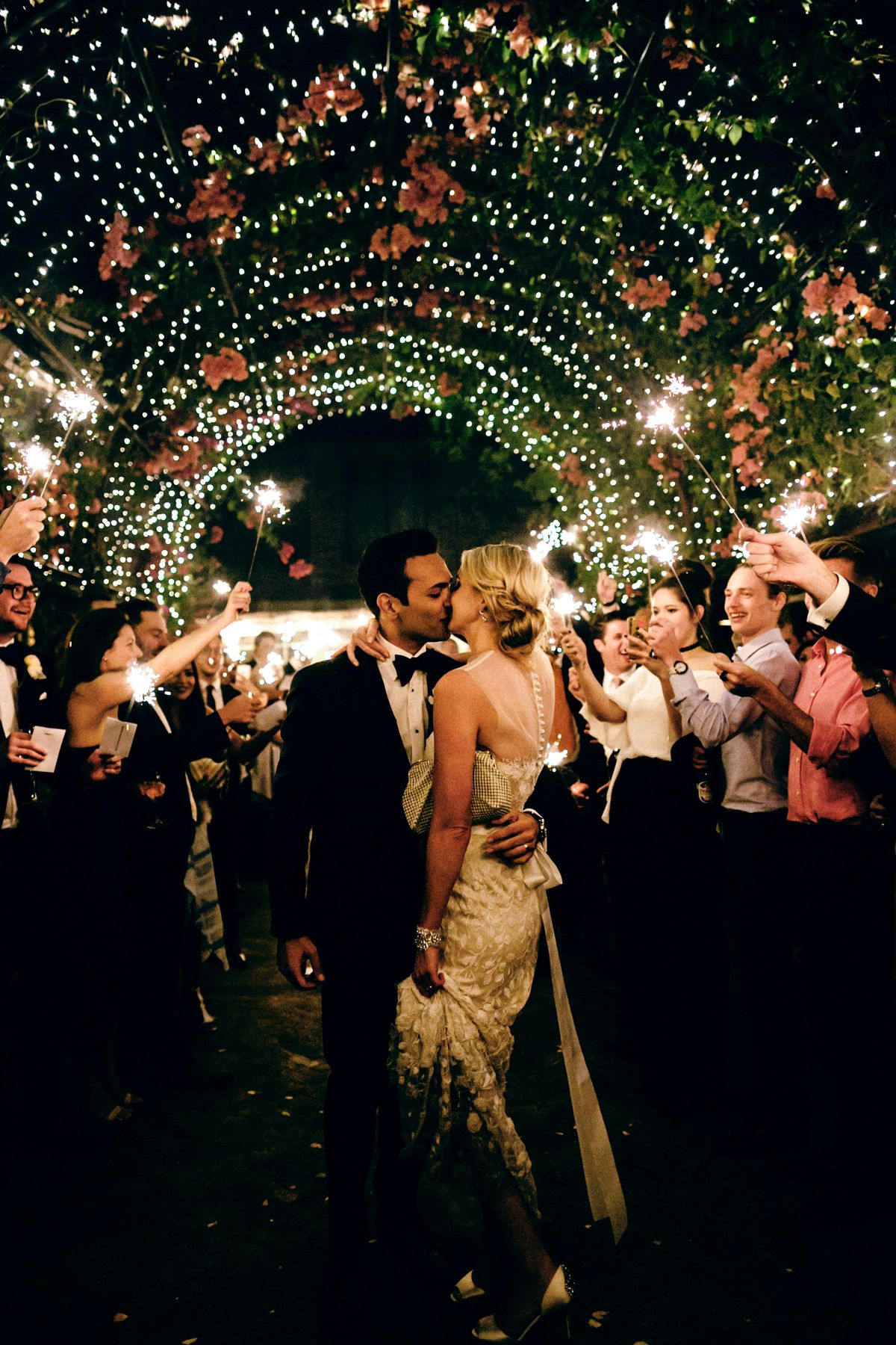 A couple kiss on their wedding day under lights and surrounded by guests