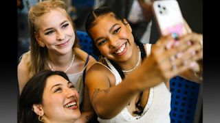 Portrait of three young woman with different skin tones smiling while taking a selfie together in a train.