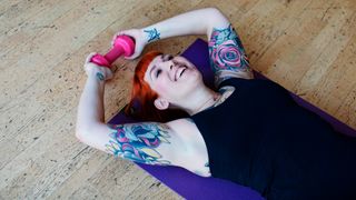 Woman lies on an exercise mat holding a dumbbell behind her head