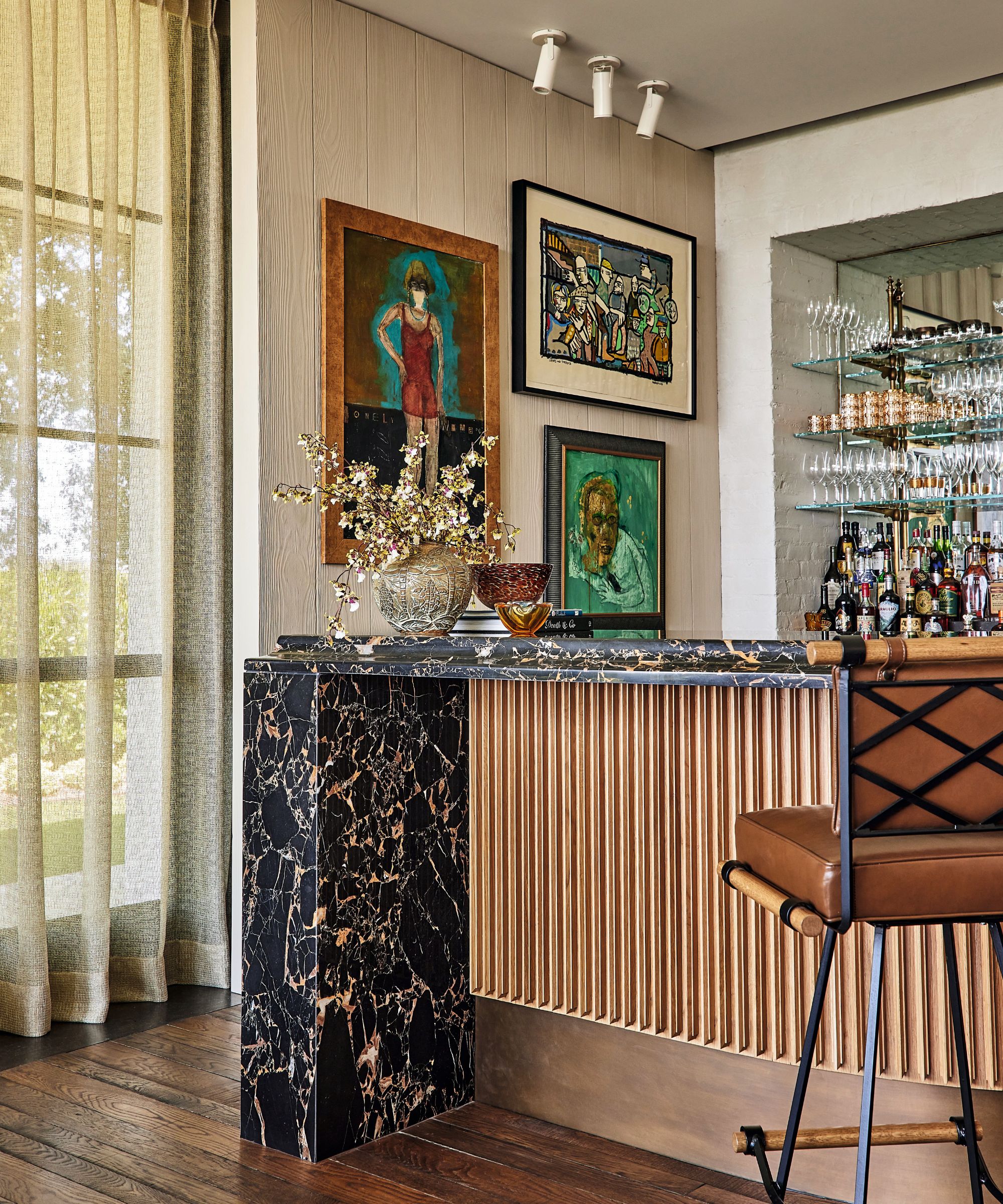 Home bar with fluted wood paneling, black marble countertop with gold veining, a leather barstool, and framed art against a paneled wall