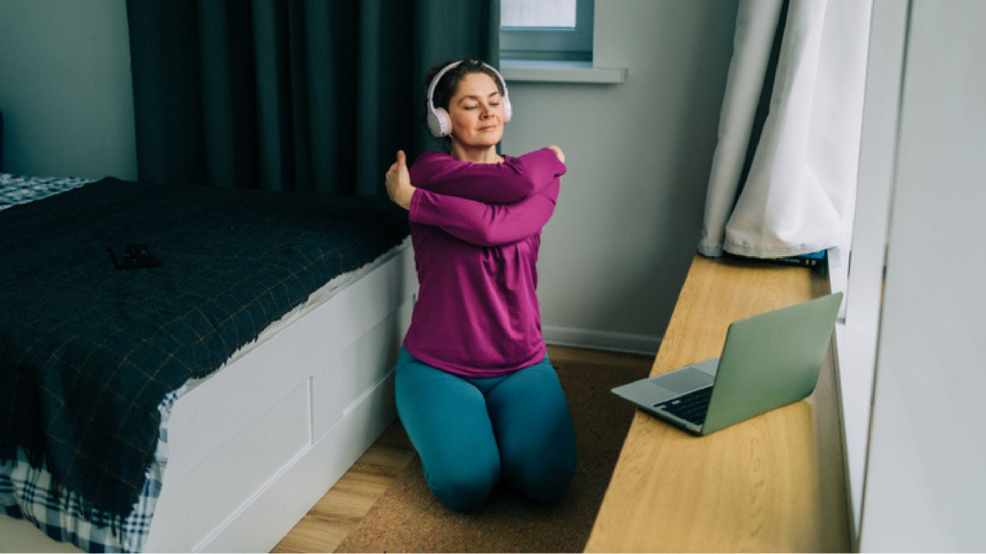 A woman wearing a pink top kneeling down doing a bear hug stretch