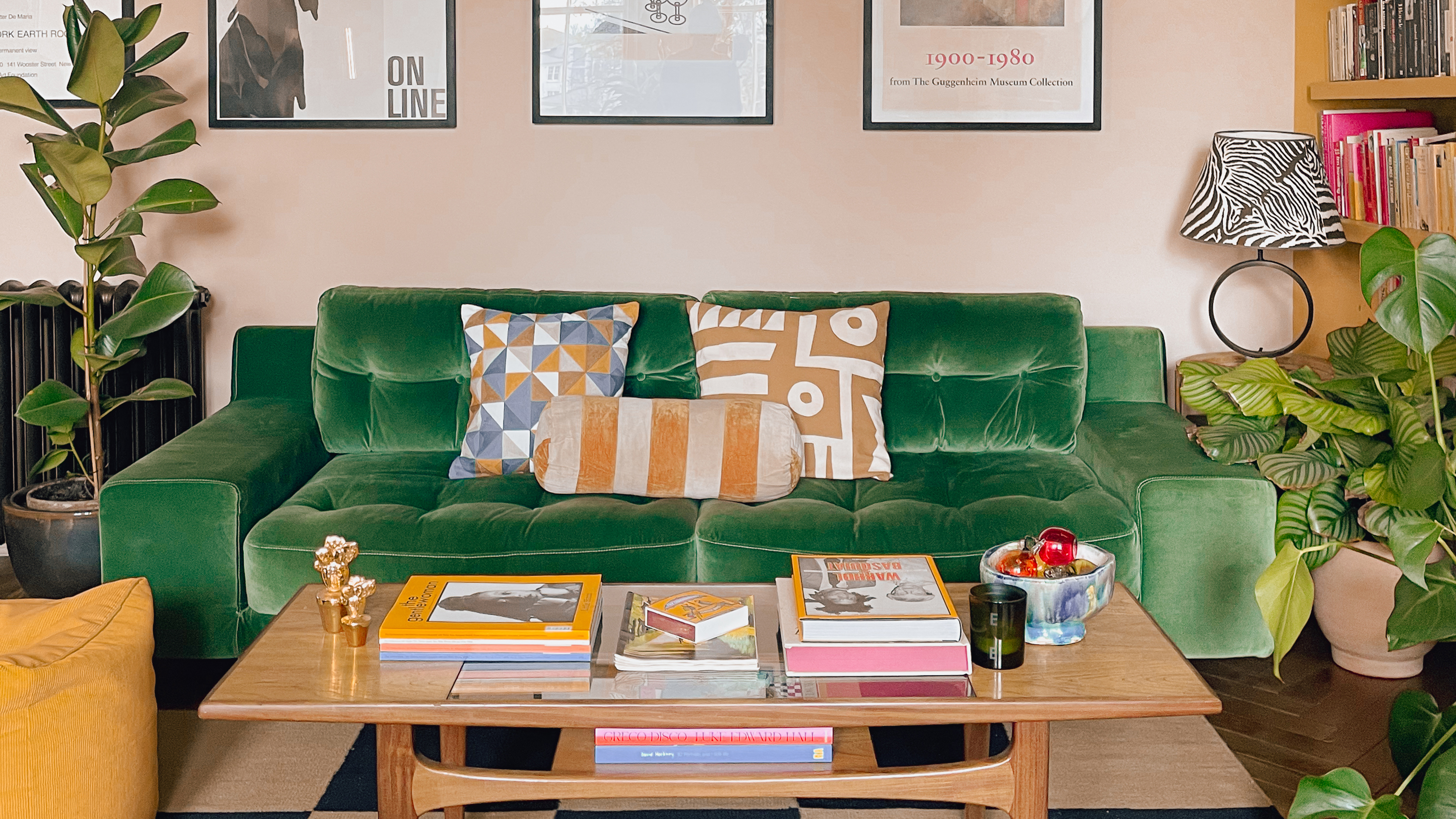 Soft pink living room with green velvet sofa and books stacked on a vintage coffee table