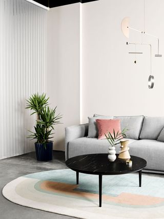 A black, round coffee table with a gray sofa, are set on a pastel-colored rug.