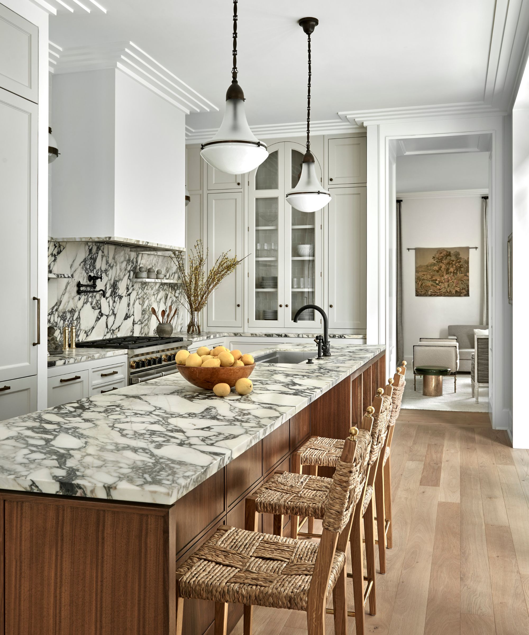 A bright kitchen featuring a large Calacatta marble island and backsplash, dark wood cabinetry, and woven rush-seat barstools.