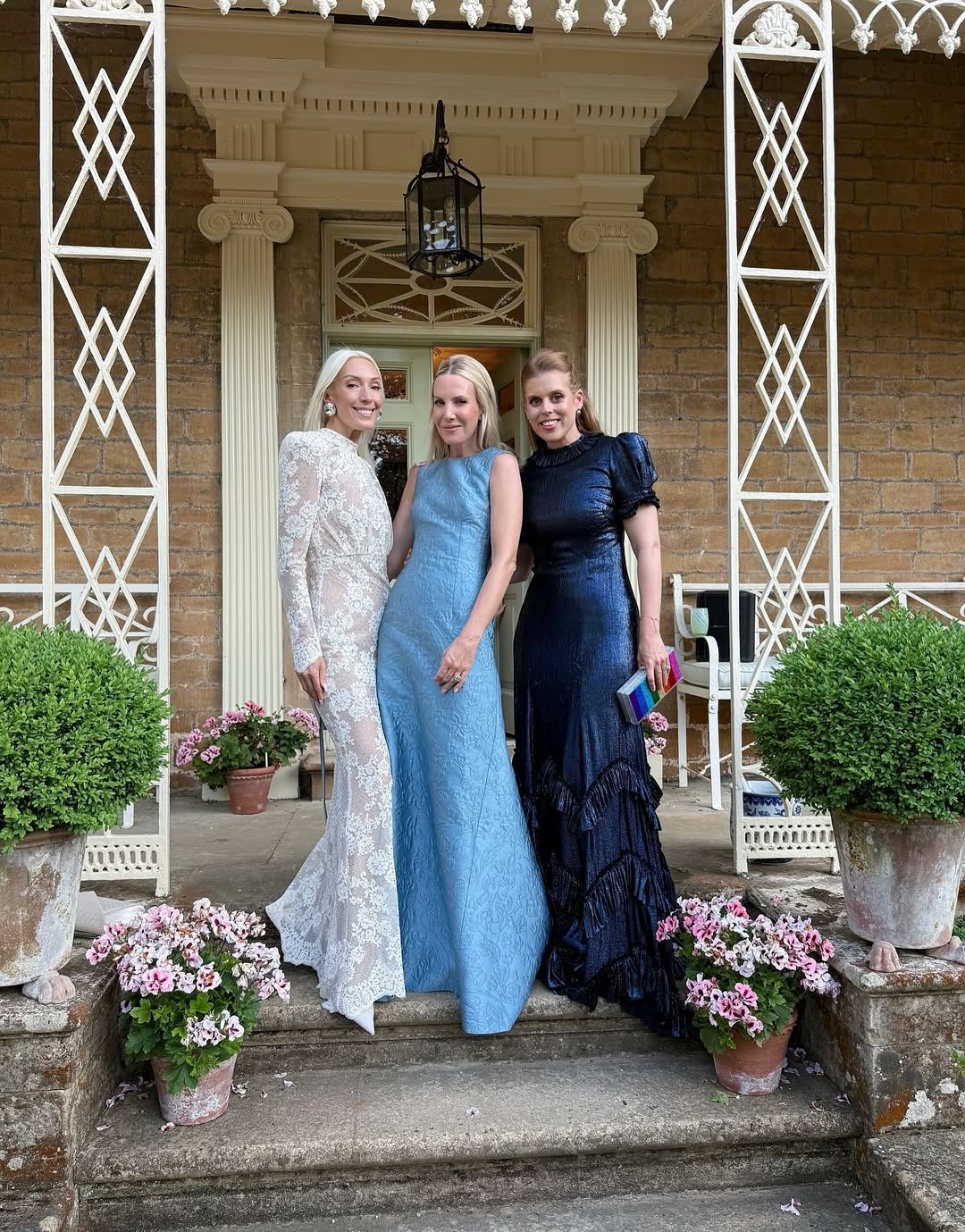 Princess Beatrice wearing a blue gown posing with Alice Naylor-Leland and Olivia Buckingham on a front step surrounded with flowers
