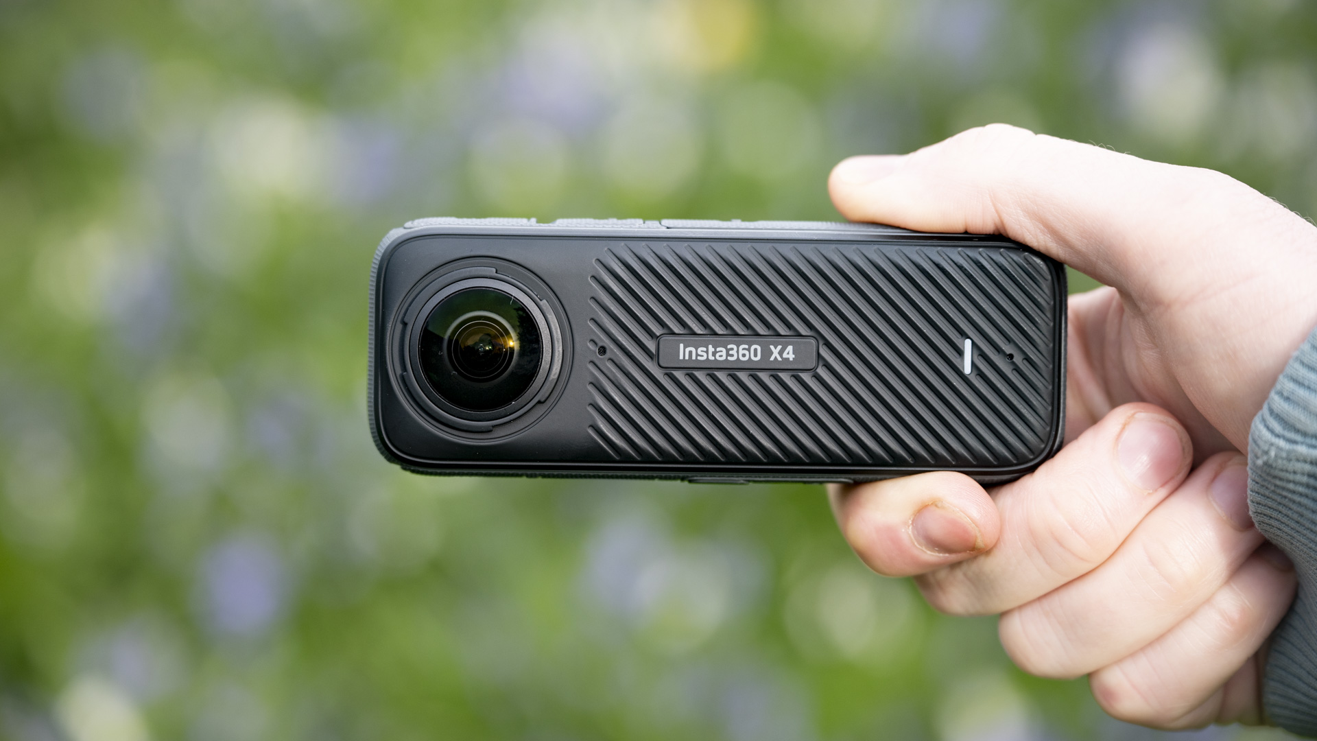 Insta360 X4 360 degree camera in the hand outdoors with vibrant grassy background