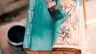 Close up of detailed wood furniture being painted teal with a paintbrush