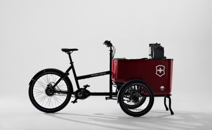 A cargo e-bike with black frame and red bin at the front with the Victorinox logo, consisting in a white cross referencing the Swiss flag